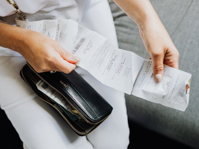 Person reviewing multiple receipts and invoices while holding a black wallet, representing tracking vacuum maintenance and replacement costs.