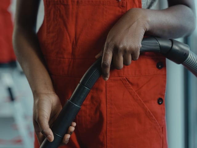 Person in red shirt holding a black vacuum hose with ribbed texture in both hands.